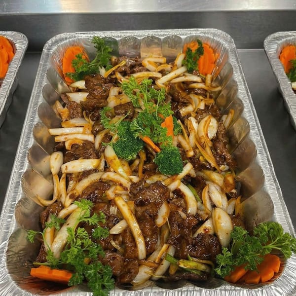 Beef and onions in a foil tray, garnished with parsley, broccoli, and carrot slices.