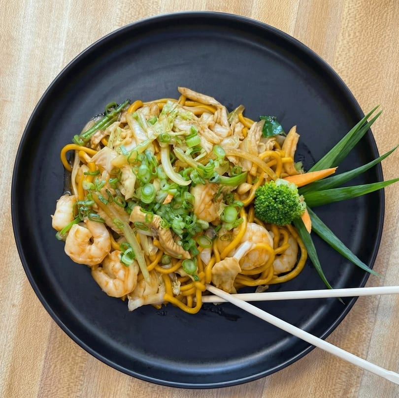 Shrimp and chicken lo mein with vegetables, garnished with broccoli, carrots, and scallions.